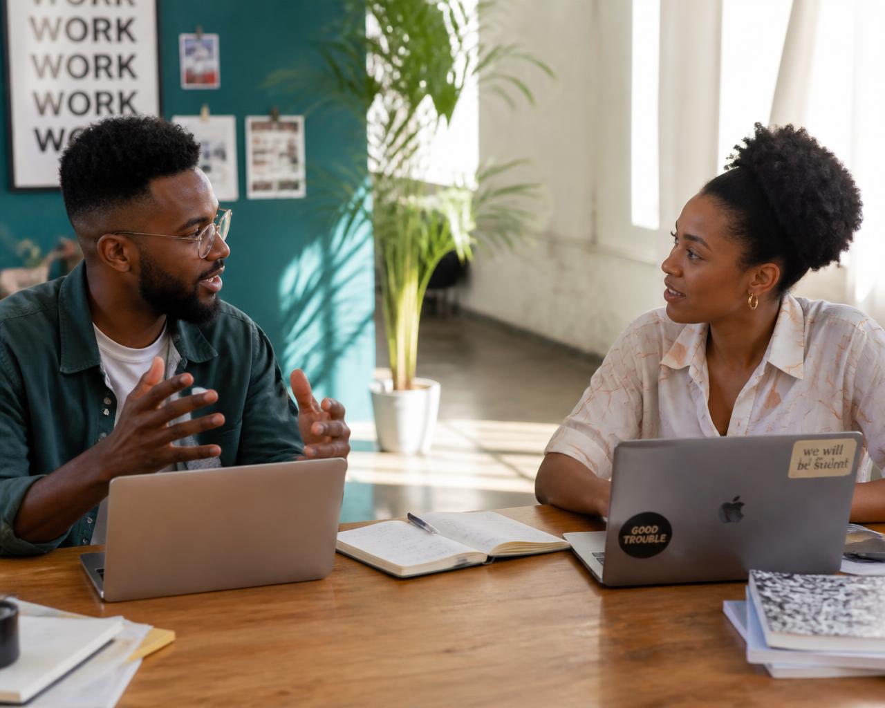 Two people collaborating over laptops and notebooks at a studio table